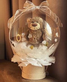 a teddy bear in a clear glass ball with white feathers and gold numbers on it