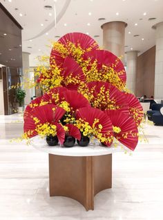 red and yellow flowers are arranged in front of a large vase with black shoes on it