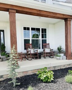 two rocking chairs on the front porch of a house with white siding and wood columns