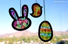 three colorful easter decorations hanging from strings in front of a window with mountains and blue sky