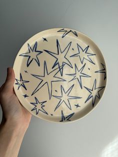 a hand holding a blue and white plate with stars on the bottom, in front of a gray wall