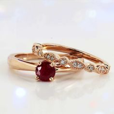 two gold wedding rings with an oval ruby stone and diamond set in the middle, on a white background