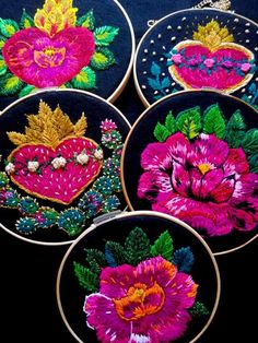 four embroidered hoops with flowers in them on a black tablecloth covered surface, one has a heart and the other has leaves