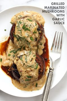 two stuffed mushrooms covered in gravy on a white plate with a fork next to it