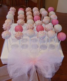 cake pops are arranged on a table with tulle bow around the edges, and pink and white frosting