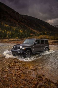 a black jeep driving through a river under a cloudy sky with mountains in the background