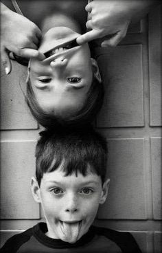 a young boy is sticking his tongue out as he sits next to an adult brushing his teeth