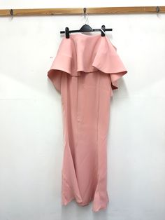 a pink dress hanging on a hanger in front of a white wall and wooden frame