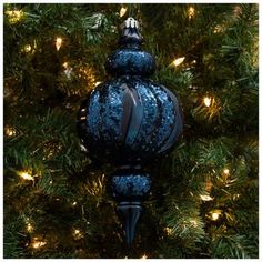 a blue ornament hanging from a christmas tree with lights on it's branches