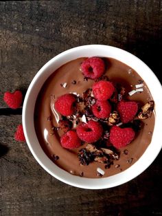 a bowl filled with chocolate and raspberries on top of a wooden table