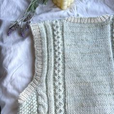 a knitted sweater next to some lavender flowers on a bed with white linens