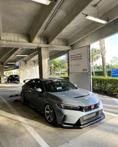 a grey car parked under an overpass in a parking lot with other cars behind it