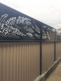 a metal fence with flowers and leaves on the top, next to a sidewalk in front of a building