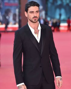 a man in a tuxedo walks down a red carpet with his hands in his pockets