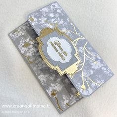 a close up of a card on a white surface with gold foil and flowers in the background