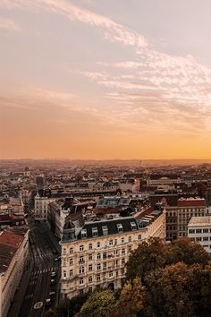 an aerial view of a city with tall buildings and trees in the foreground at sunset