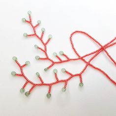 two red string art pieces with green beads on white surface, one is shaped like branches and the other has leaves