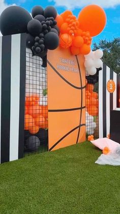 an outdoor basketball themed birthday party with balloons and streamers on the wall, in front of a fence