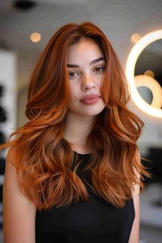 Woman with long, wavy, auburn hair standing in a modern salon. Red And Brunette, Auburn Hair Ideas