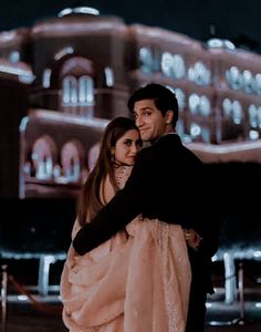 a man and woman standing next to each other in front of a building at night