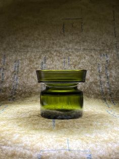 a green glass jar sitting on top of a white tablecloth covered floor next to a wall