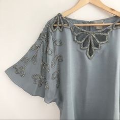 This Blouse Is Gorgeous! Beautiful Bead Work At Neckline, Down Flutter Sleeves & Back Of Neck Cut Out. Single Eye Hook Closure In Back. Color Is Smoke Star Which Is A Light Gray. Beads Are A Gray Iridescent Color. When Light Shines On Them You Can See Many Beautiful Colors. Content Is 100% Viscose (Silk). Measurements Flat Are Approximately 22” Pit To Pit & 28” Long. In New Condition With A Small Flaw In Material On Back Of Blouse. See Last Photo. Nwt (Box H-10) Elegant Embellished Short Sleeve Blouse, Elegant Beaded Short Sleeve Tops, Elegant Embellished Silver Blouse, Elegant Short Sleeve Embellished Blouse, Elegant Silver Embellished Blouse, Elegant Silver Beaded Tops, Silver Embellished Tops For Wedding, Batwing Sleeve Top, Flutter Sleeve Blouse