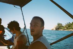 two men sitting on a boat in the water, one looking at the camera while the other looks off to the side