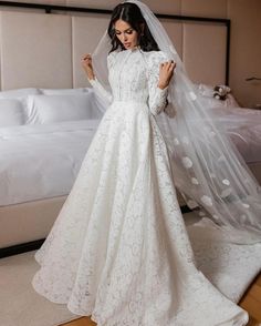 a woman wearing a wedding dress and veil standing in front of a bed with her hands on her hips