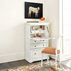 a white desk and chair with a cow painting on the wall above it in a room