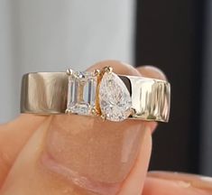 a close up of a person's hand holding a ring with two diamonds on it