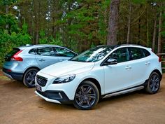 two white cars parked next to each other on a dirt road in front of trees