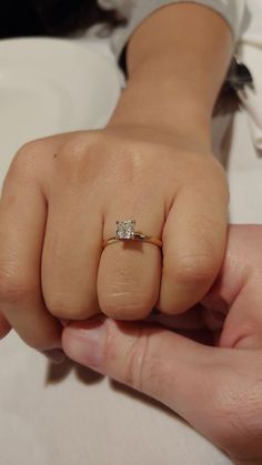 a close up of a person's hand holding a ring with a diamond on it