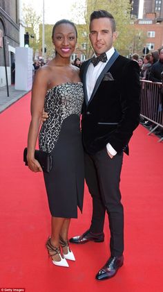 two people standing on a red carpet posing for the camera with one person in a tuxedo