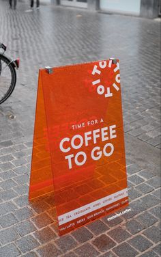 an orange sign sitting on the side of a brick road next to a black bike