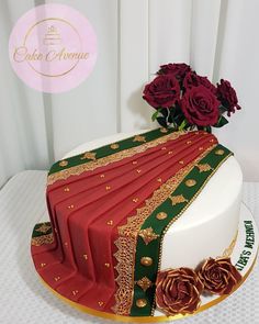 a red and green cake with roses on top is sitting on a white tablecloth