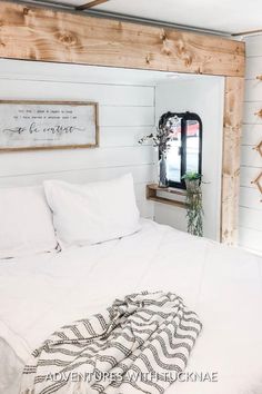 a bed with white sheets and pillows in a bedroom next to a mirror on the wall