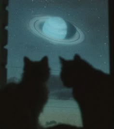 two cats are looking out the window at an object in the sky that looks like saturn