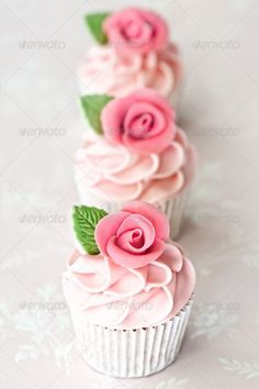 three cupcakes with pink frosting and green leaves on the top one is decorated with roses