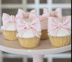 three cupcakes with pink bows are sitting on a cake plate