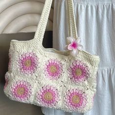 a crocheted purse with pink and white flowers on the front, hanging from a hook