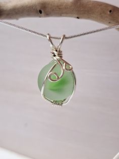 a green sea glass pendant hangs from a silver chain on a white surface with a tree branch in the background