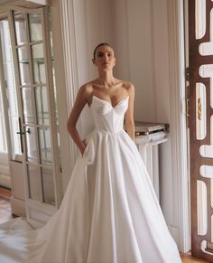 a woman in a white wedding dress standing next to a door with her hands on her hips