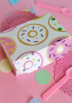 a pink table topped with lots of donuts on top of paper and plastic utensils