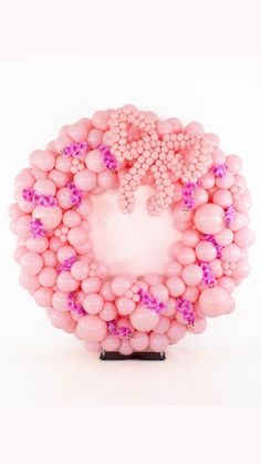 pink balloons arranged in the shape of a wreath on top of a black stand against a white background