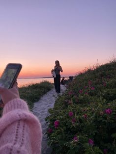 a woman taking a photo with her cell phone on the path to the beach at sunset