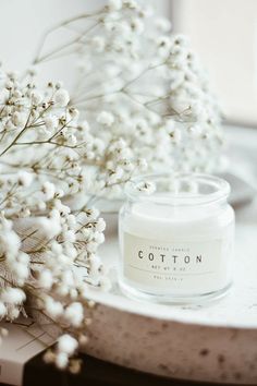 a white candle sitting on top of a table next to flowers and a vase filled with baby's breath