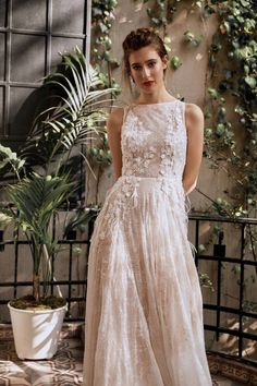 a woman in a white dress standing next to a plant