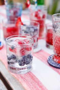 a table topped with glasses filled with water and berries on top of each other in front of a red white and blue checkered table cloth