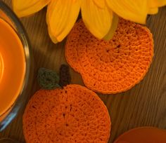 two crocheted pumpkins sitting next to a yellow candle and some flowers on a table