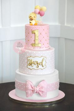 a three tiered cake with pink and white polka dots, gold foil lettering and a duck on top